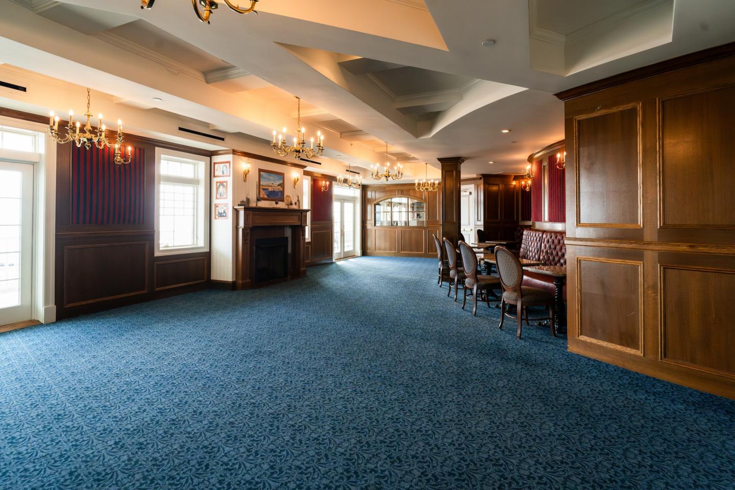 Spacious, elegant room with chandeliers and blue carpet, featuring wooden paneling.
