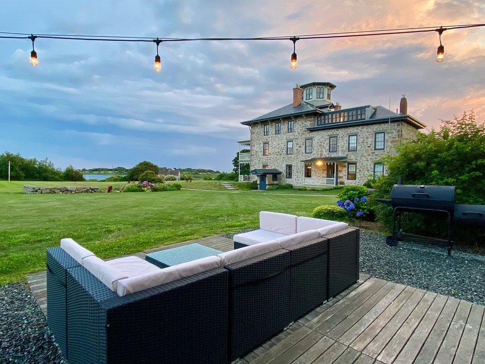 Patio with sofas, string lights, large house, and lawn at sunset.