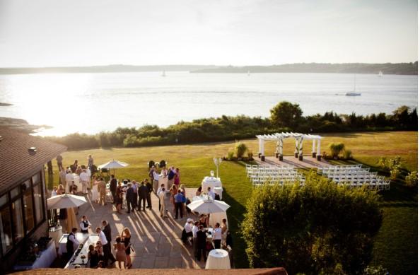 Outdoor wedding with guests by a lakeside, arbor, and sunny sky.