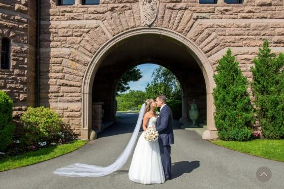 Bride and groom kissing under a stone archway.