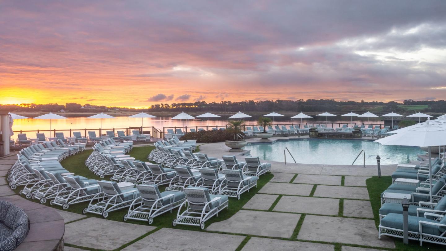 Poolside lounge chairs and umbrellas at sunset, with scenic lakeside view.