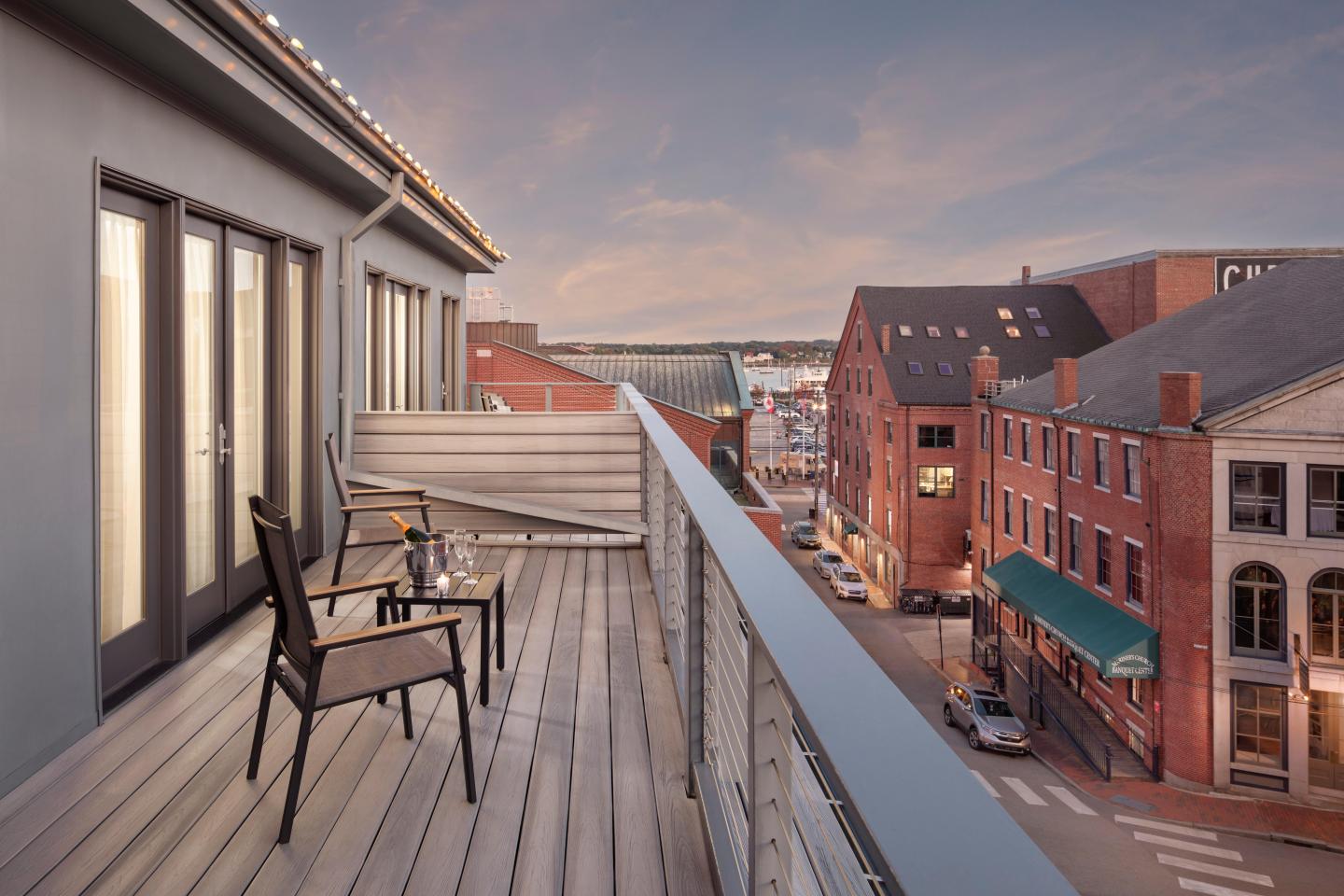 Off-room deck with chairs, city street view at sunset, warm colors.