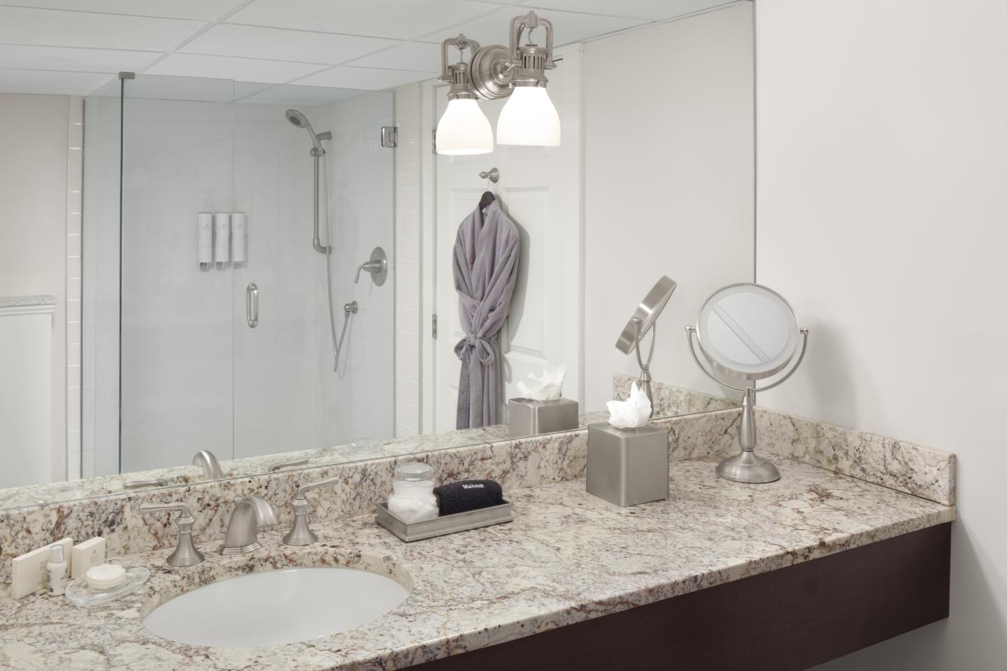 Bathroom with granite sink counter, mirror, robe, and glass shower.