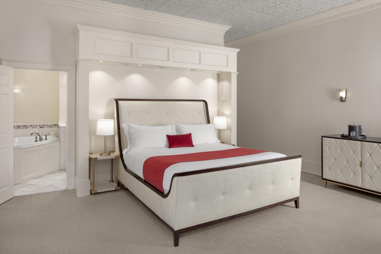 Elegant hotel room with a white bed, red accents, and an open door to a bathroom.