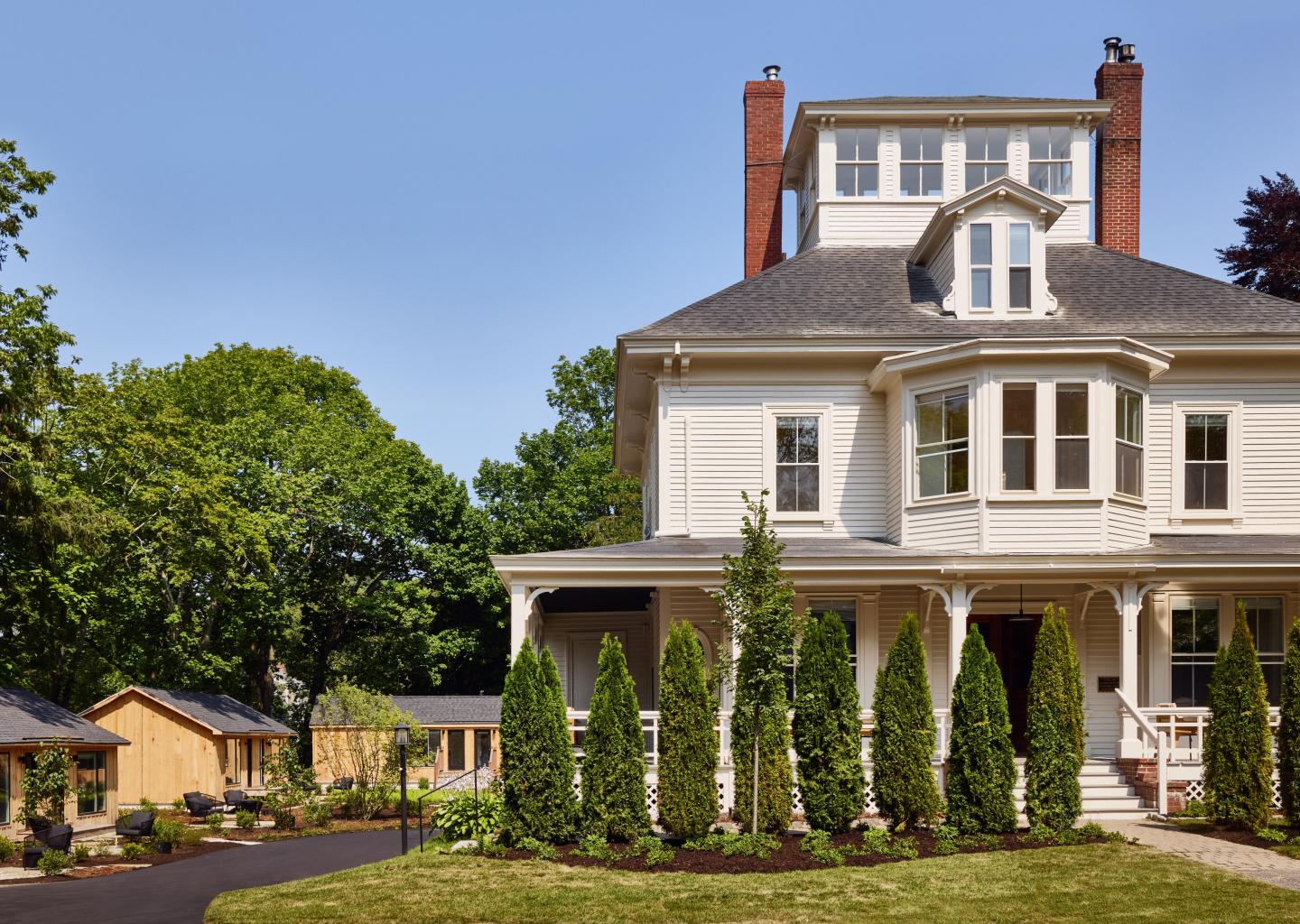 Large white house with a porch, surrounded by tall trees and a manicured lawn.