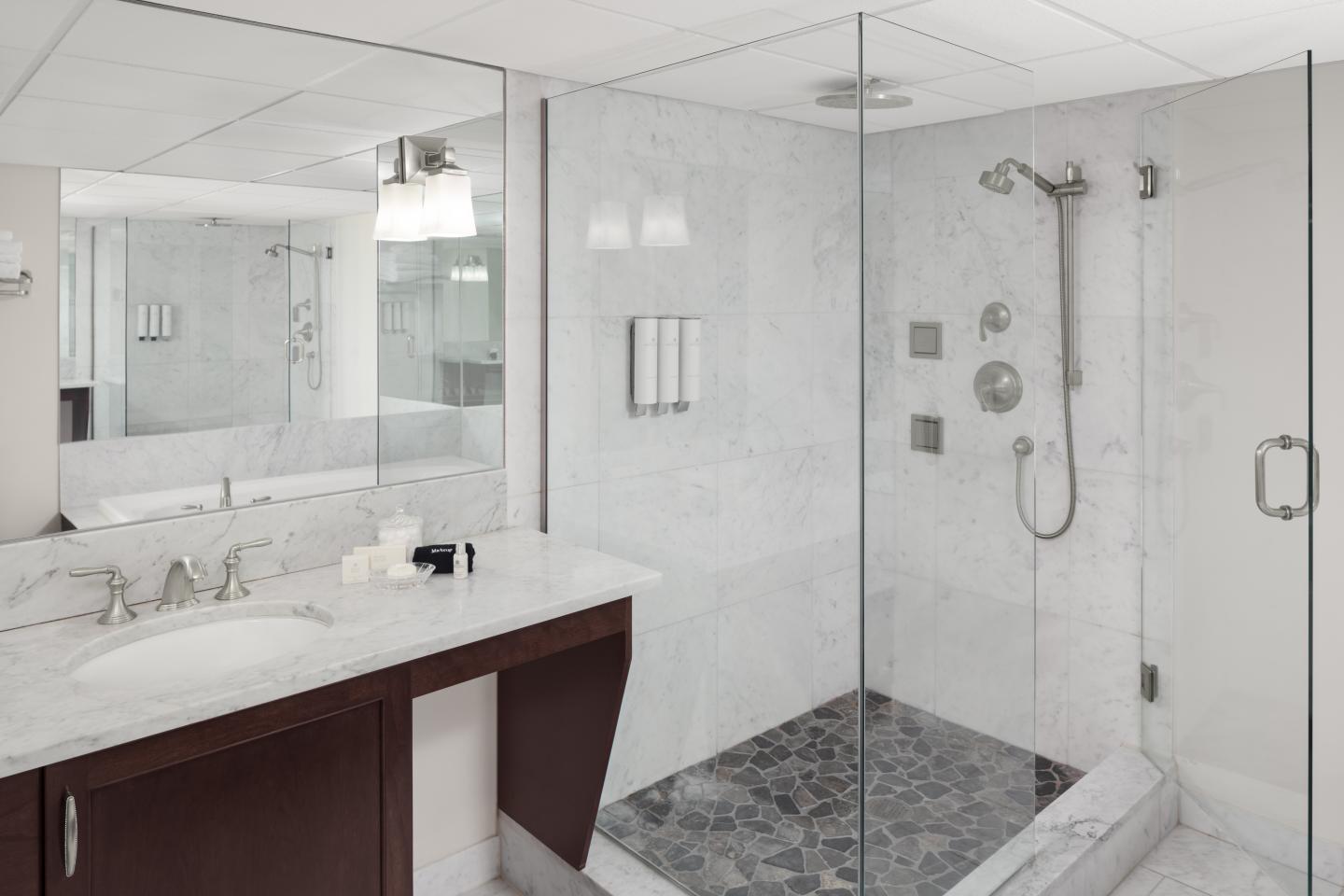 Modern bathroom with glass shower, marble tiles, and dark wood vanity.