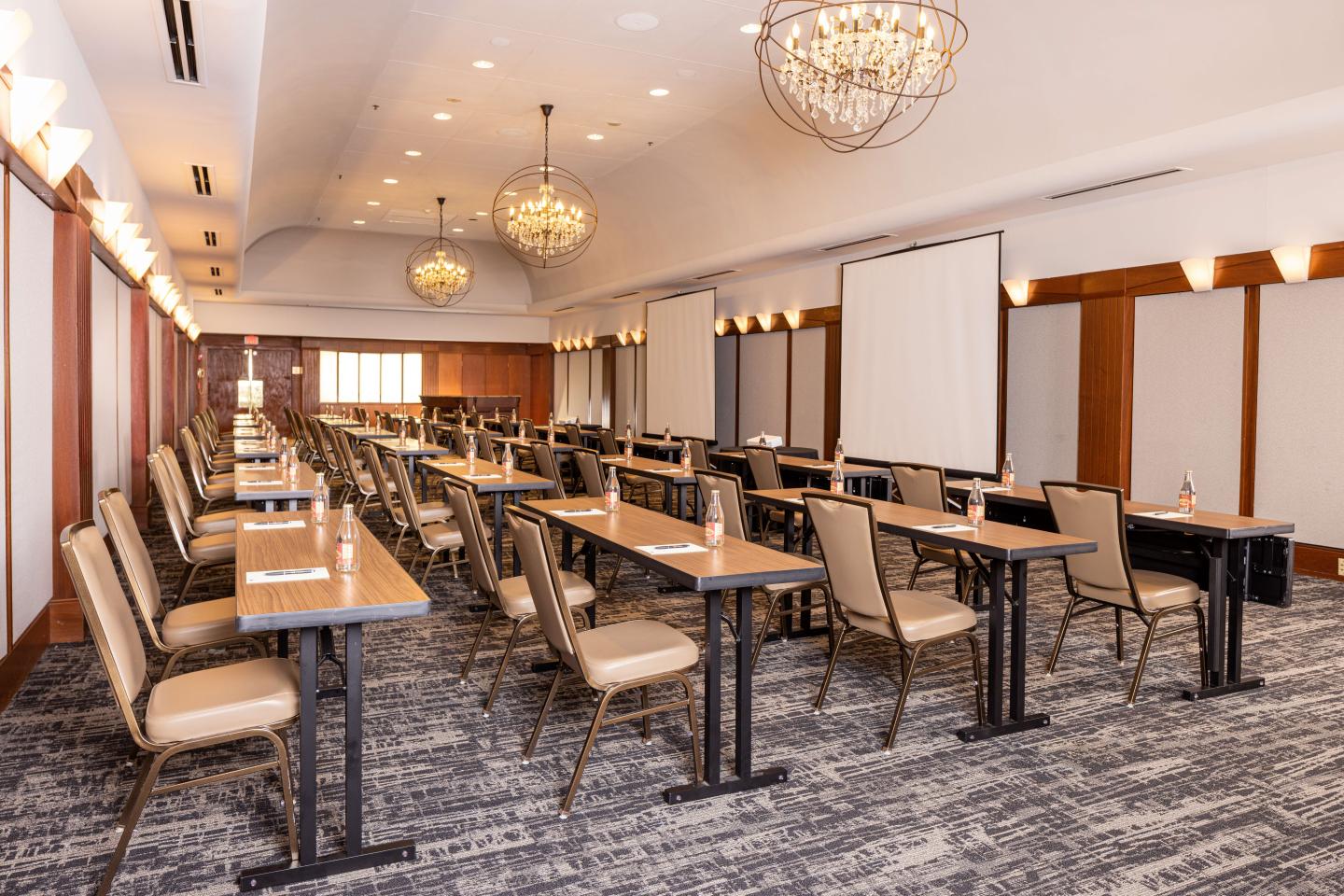 Conference room with empty rows of tables and chairs, chandeliers above.