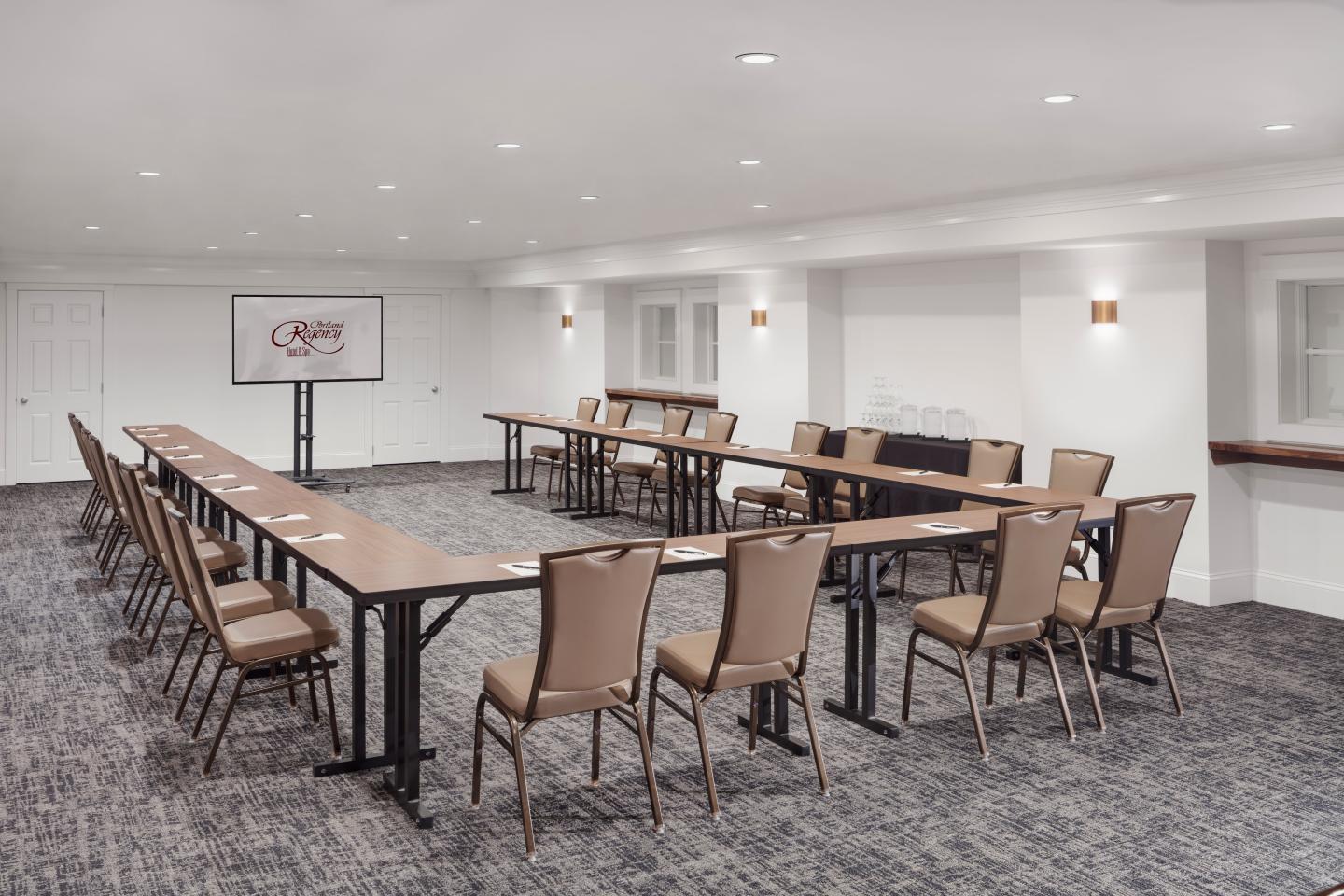 Meeting room with U-shaped table and beige chairs, screen at front.
