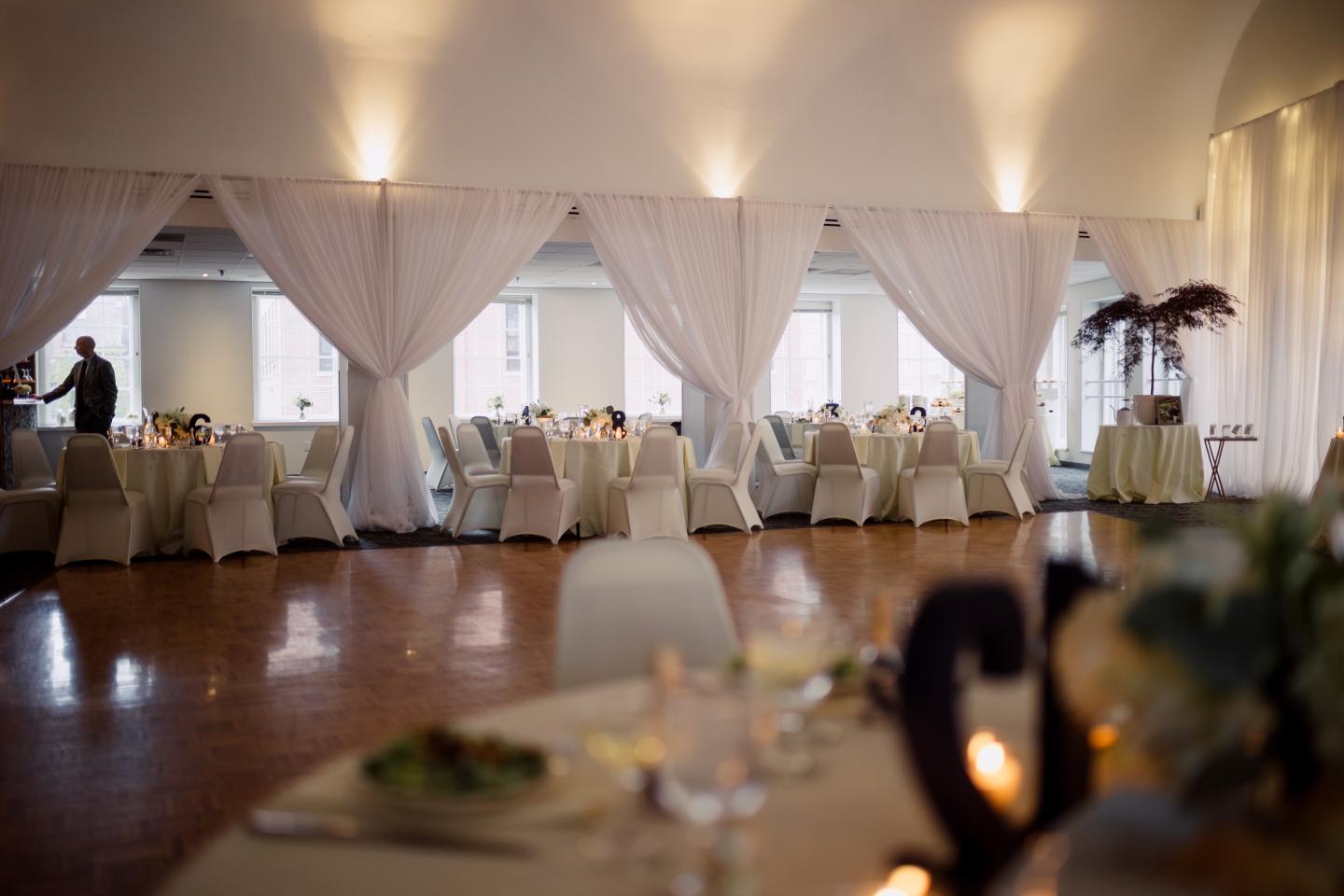 Elegant banquet hall with round tables, white drapes, and soft lighting.
