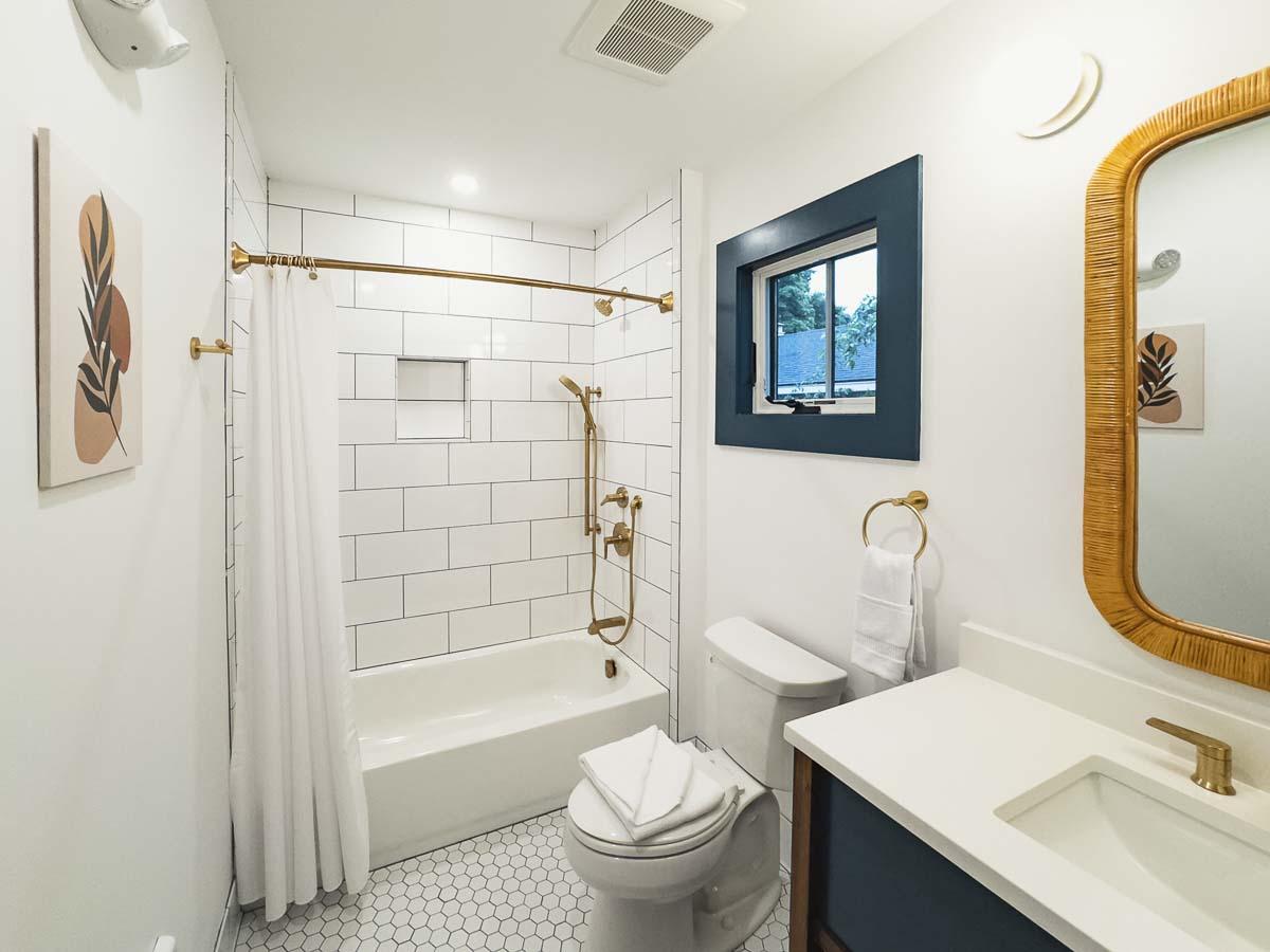 Bright bathroom with white tiles, gold fixtures, and woven mirror frame.