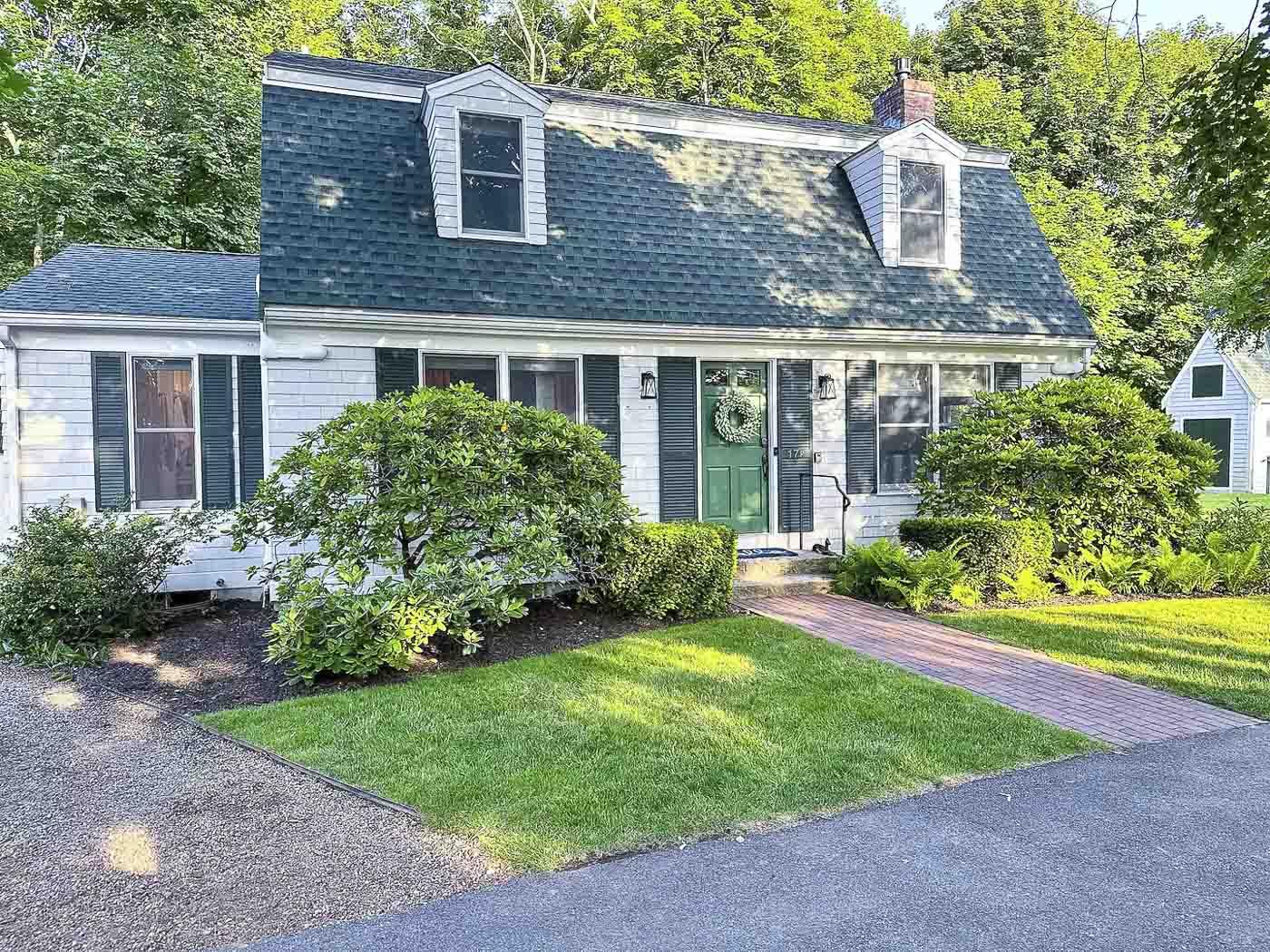 Green-roofed house with white exterior and manicured lawn, surrounded by trees.