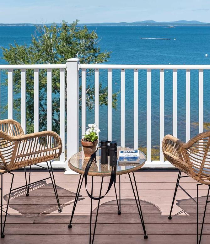 Chairs and table on a deck overlooking a blue sea with distant hills.