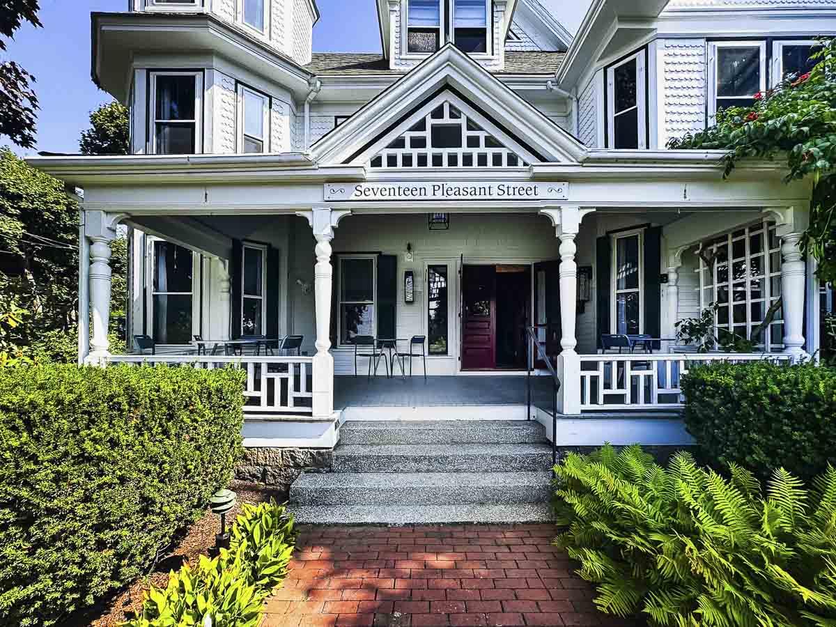 Victorian-style house with a large porch and manicured shrubs.