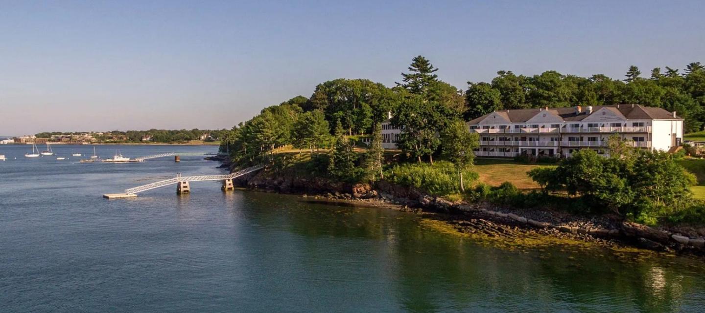 Coastal landscape with a large white house by the water, surrounded by greenery.