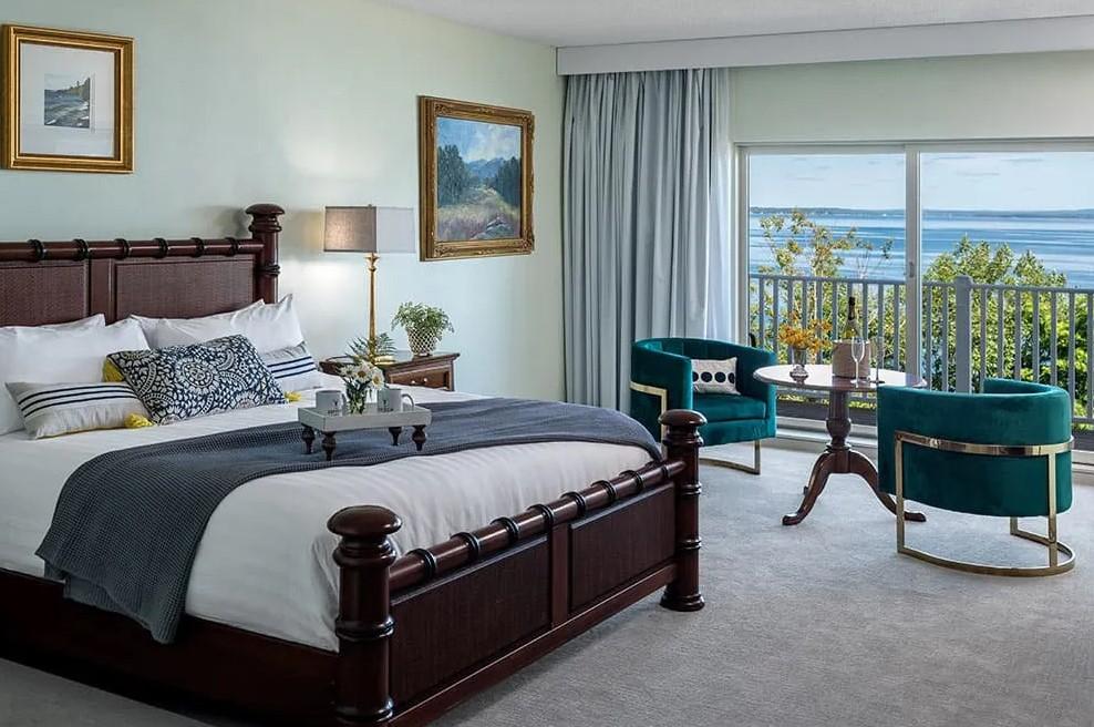 Elegant hotel room with a sea view, large bed, teal chairs, and soft lighting.