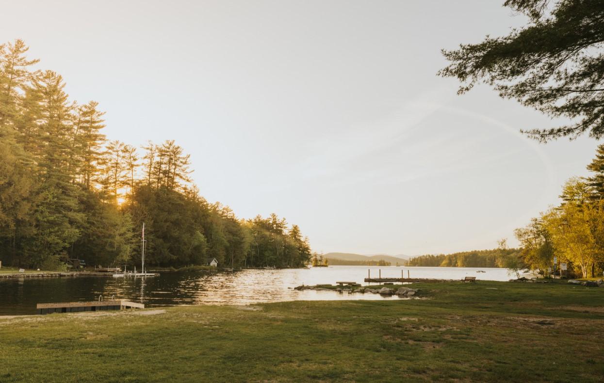Tranquil lakeside at sunset with trees and a dock.