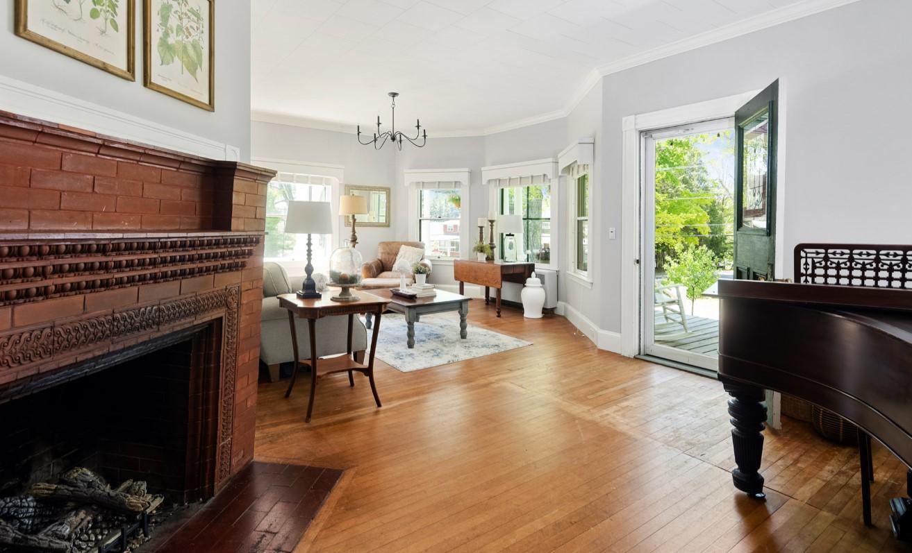 Elegant living room with wooden floors, a red brick fireplace, and large windows opening to a garden.