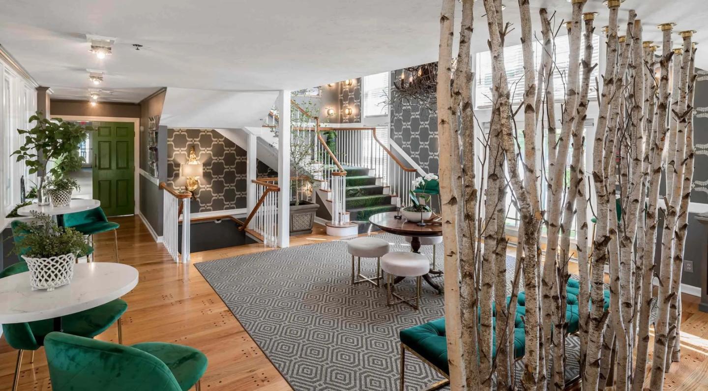 Modern hotel lobby with birch tree divider, green chairs, and decorative staircase.by