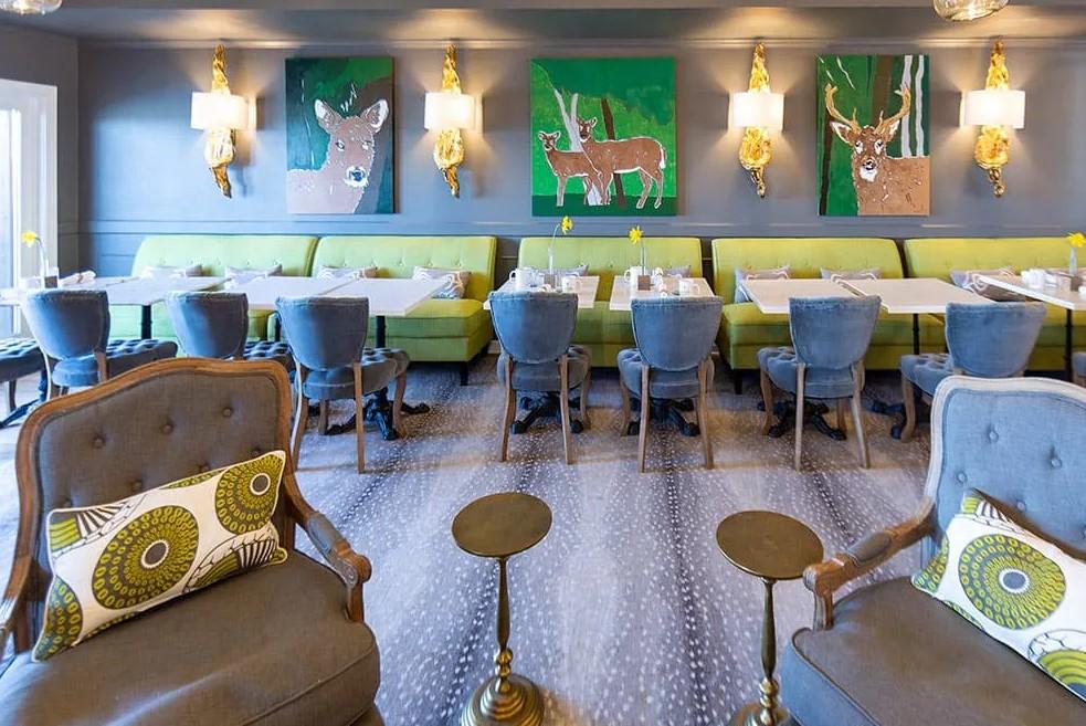 Modern restaurant with green sofas, blue chairs, and animal paintings.