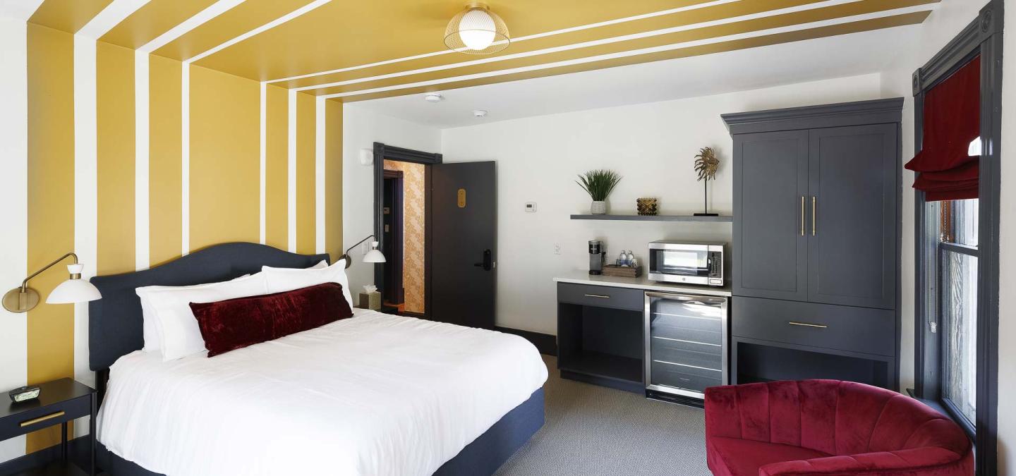 Hotel room with a double bed, kitchenette, and yellow-striped walls.