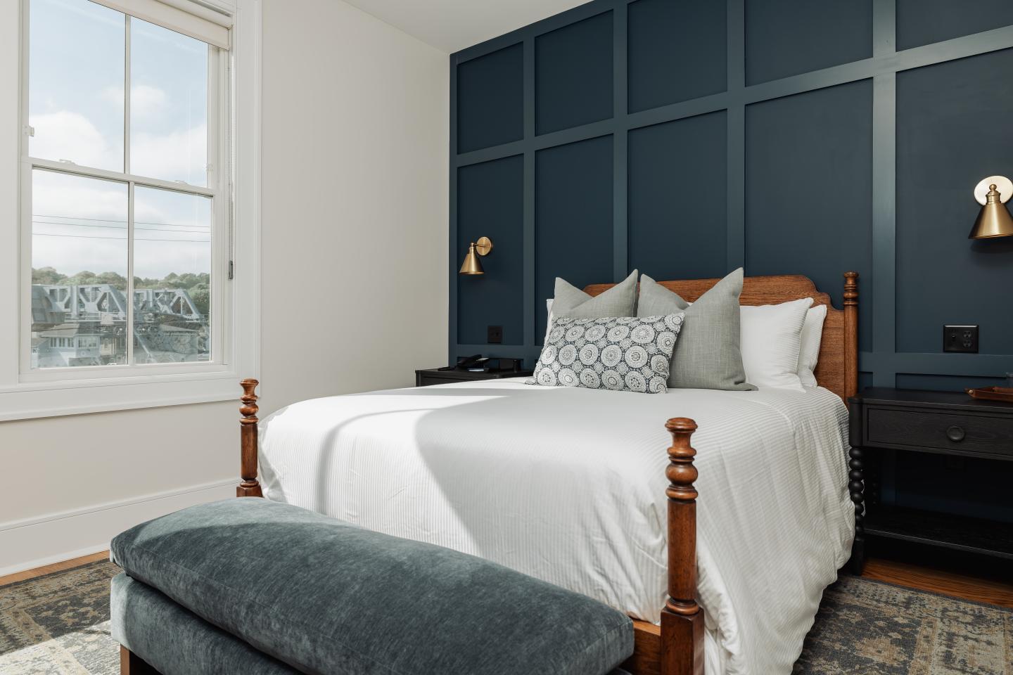 Cozy bedroom with a white bed, blue accent wall, and natural light from a window.