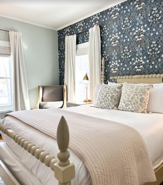 Cozy bedroom with floral wallpaper, bed, and armchair. Bright lighting.