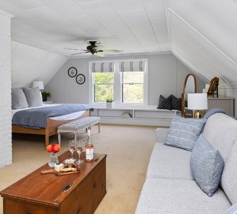 Cozy attic bedroom with a bed, sofa, and coffee table. White walls and ceiling fan.