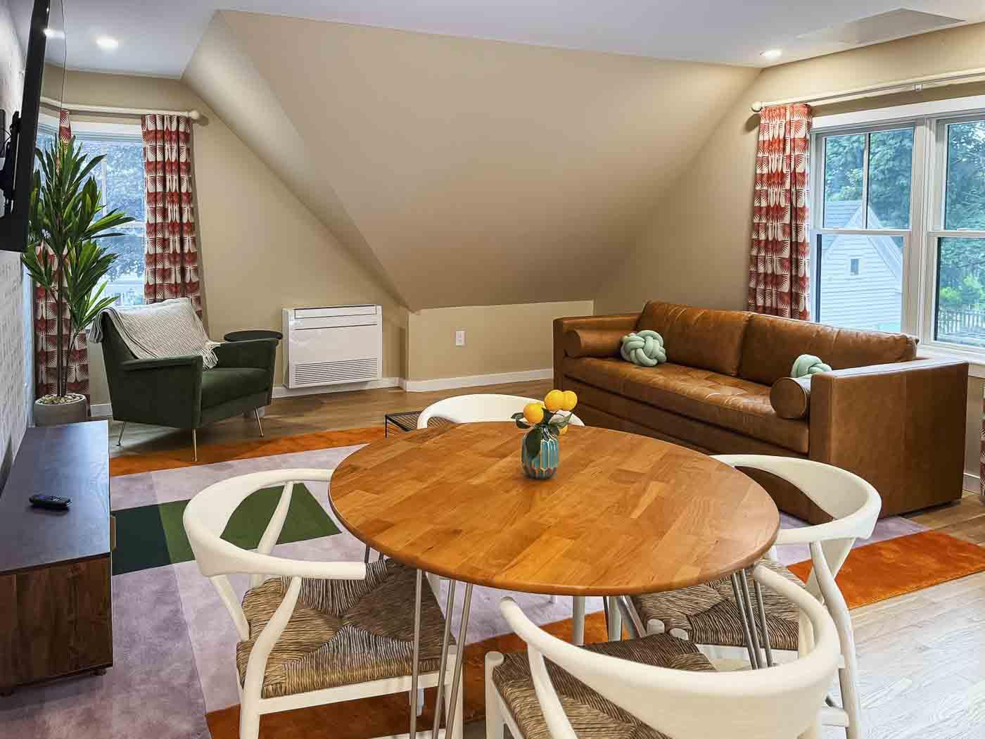 Cozy living room with round wooden table, chairs, sofa, and large windows.