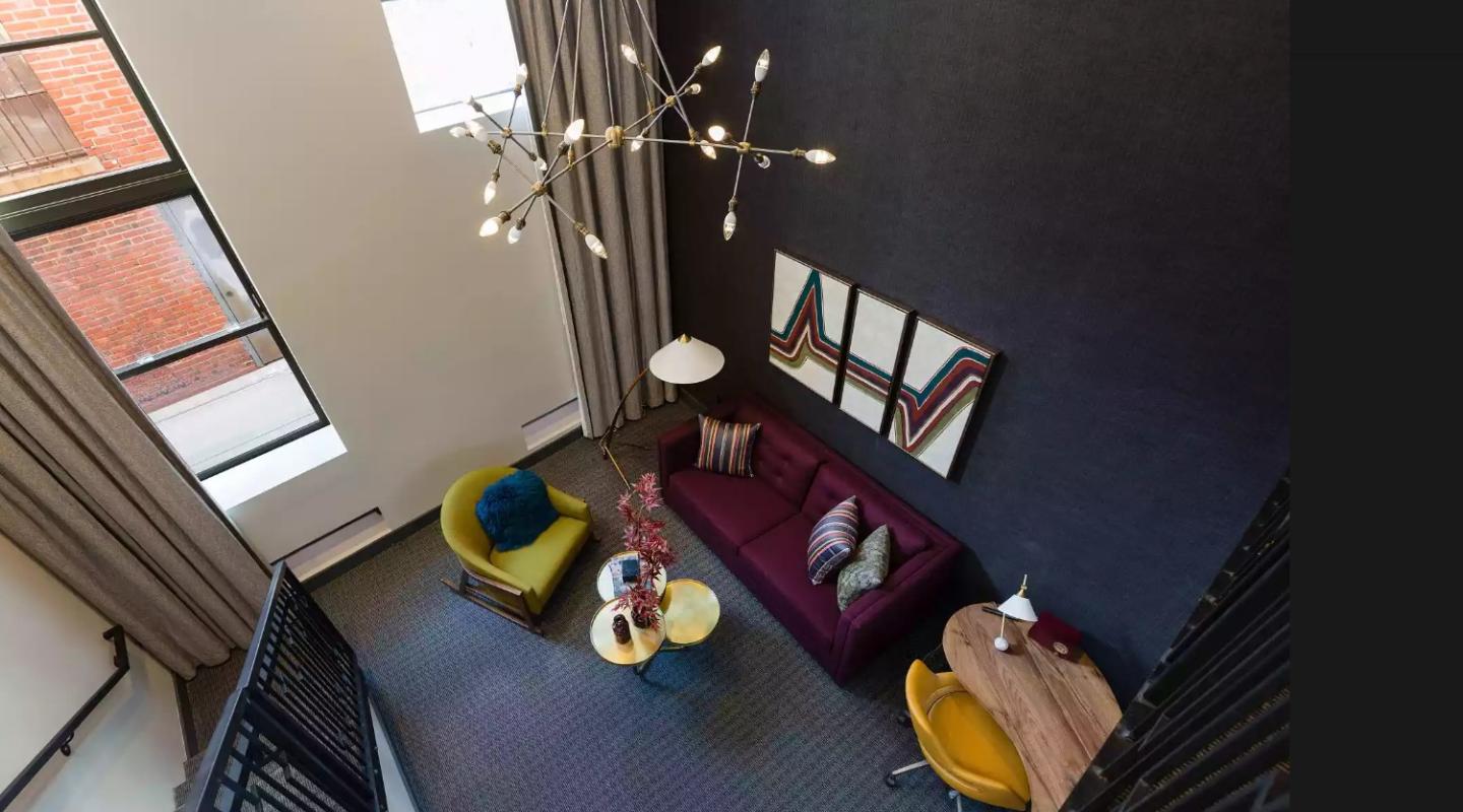 Modern living room with purple sofa, bright chairs, and abstract art.