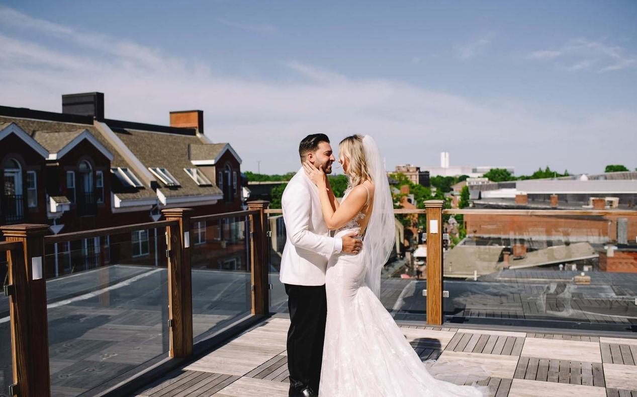 Bride and groom smiling on a sunny rooftop with city view.