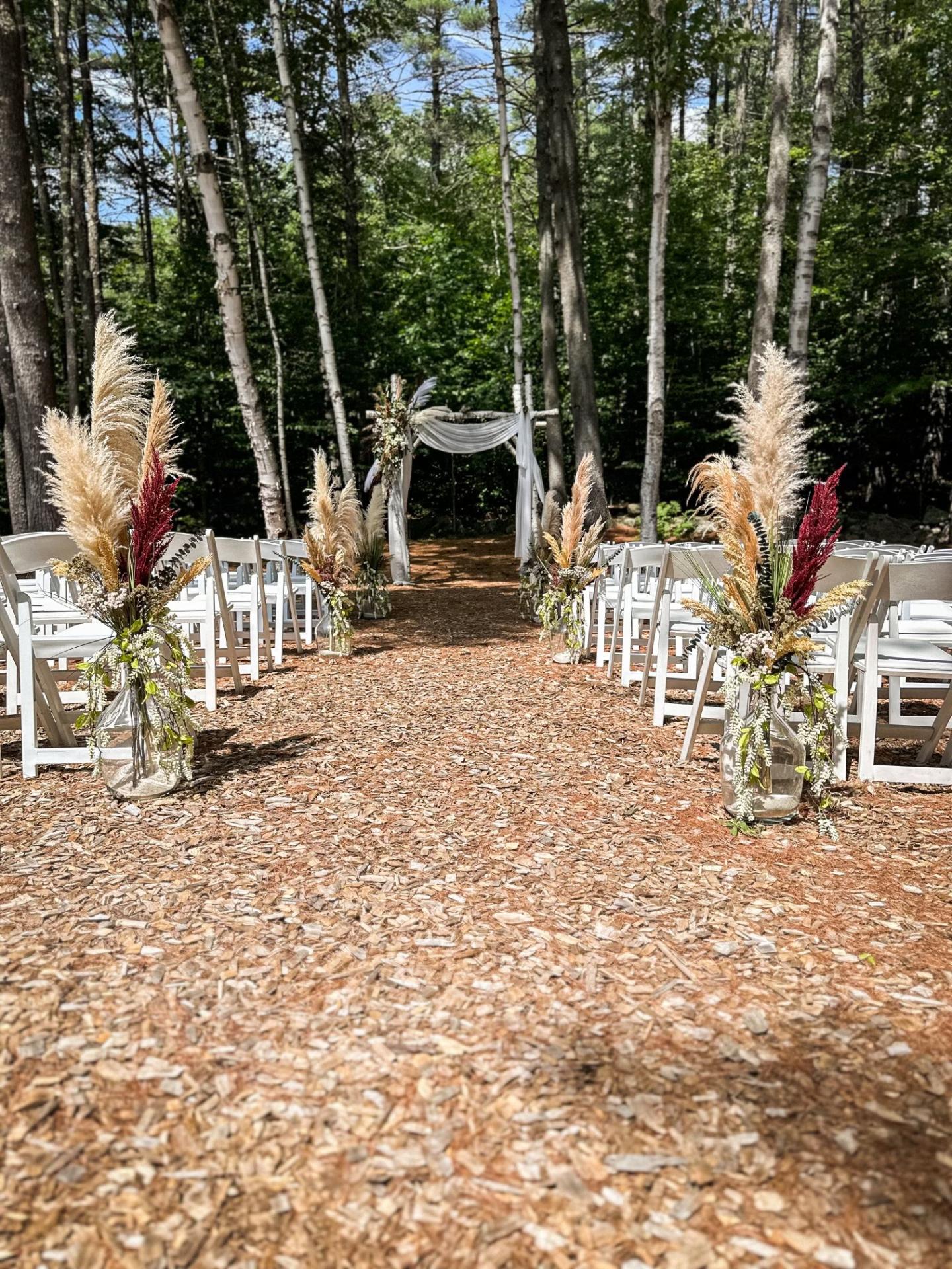 Forest wedding setup with white chairs and floral aisle decor.