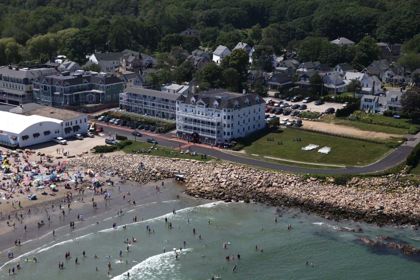 Aerial view of a crowded beach with adjacent buildings and greenery.