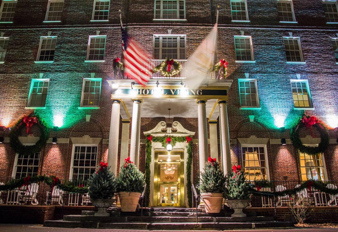 Historic hotel entrance adorned with wreaths and flags, illuminated at night.