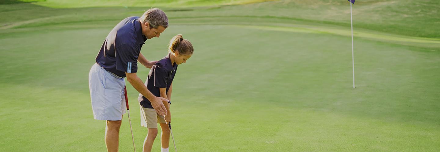 Man helping child with golf swing on a green course.