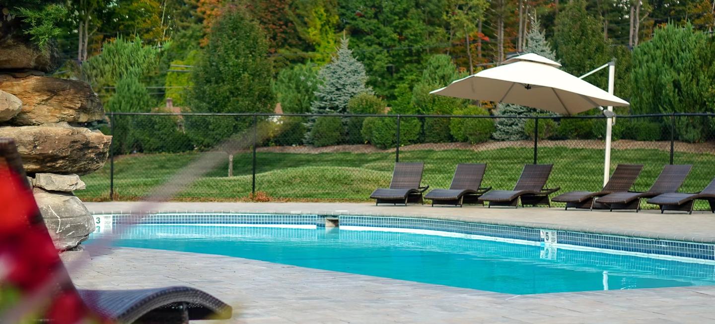 Poolside loungers with umbrella in a lush garden setting.