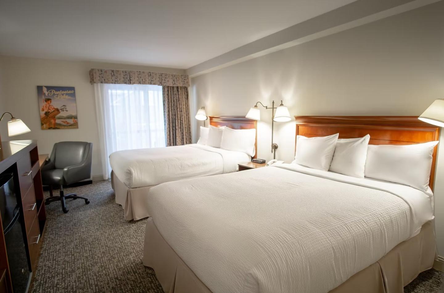 Two double beds in a hotel room with a desk and chair.