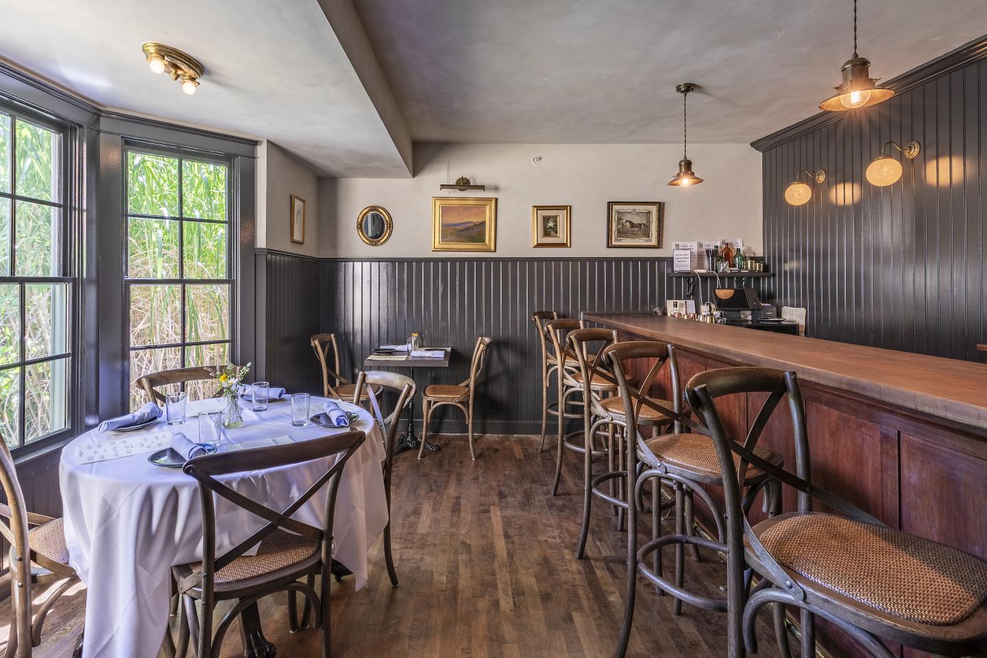 Cozy tavern interior with wooden chairs and tables by large windows.