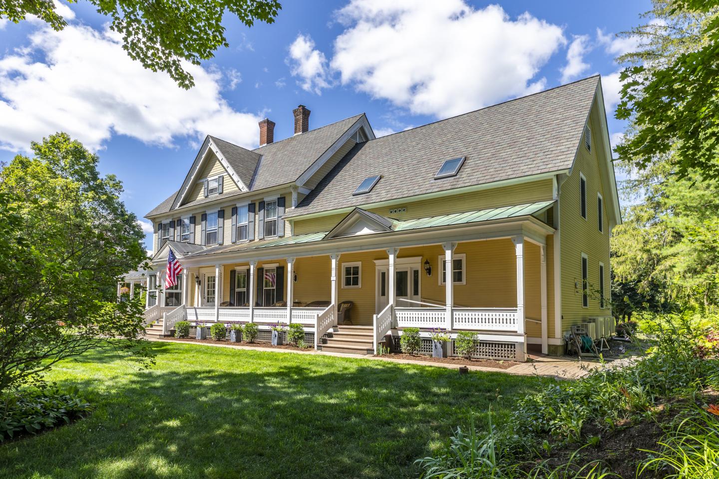 Yellow inn building with a large porch, surrounded by greenery under a bright blue sky.