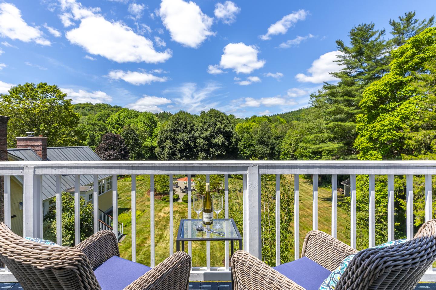 Two wicker chairs on a balcony overlook a lush green landscape under a blue sky.