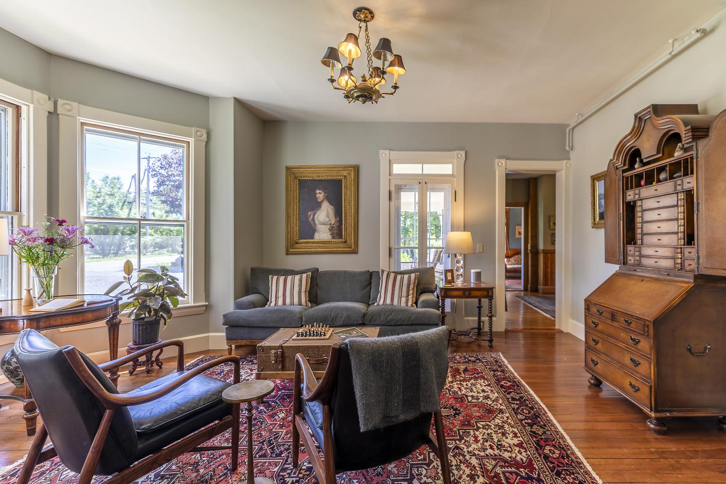 Elegant living room with vintage furniture, portrait, and large windows.
