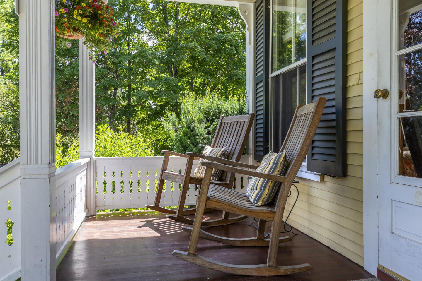 Two wooden rocking chairs on a sunny porch with plants.
