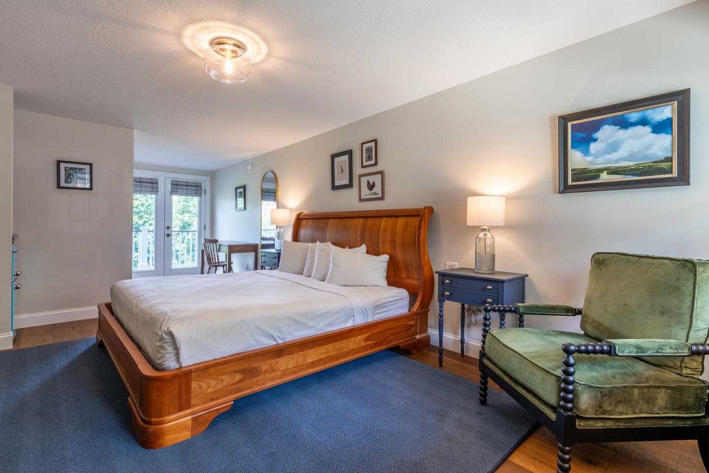 Spacious bedroom with a wooden bed, green armchair, and paintings on the walls.