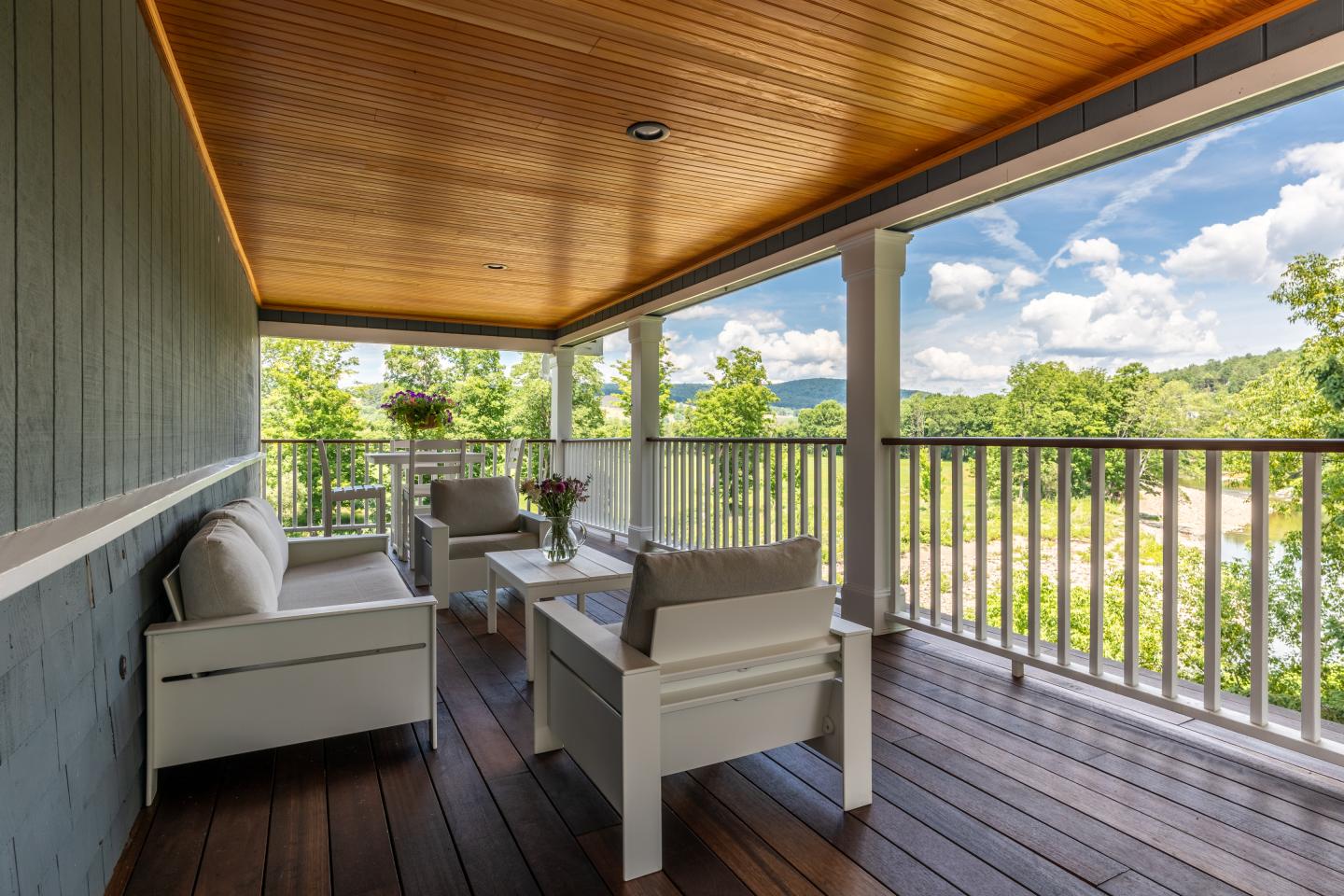 Covered porch with white seating, wooden ceiling, and a scenic mountain view.