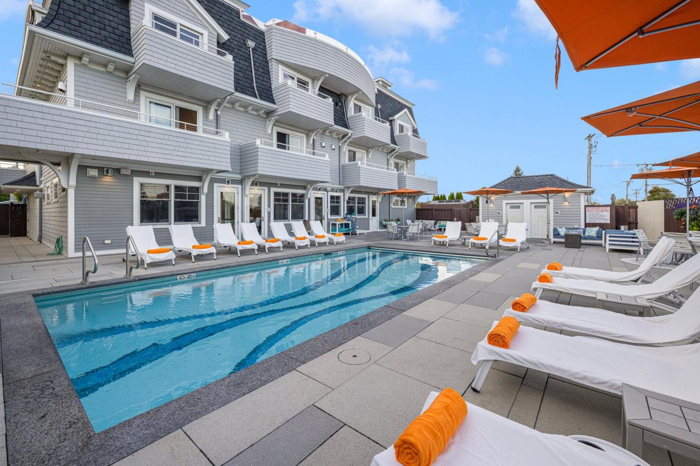 Sunny hotel pool with loungers, orange towels, and umbrellas.