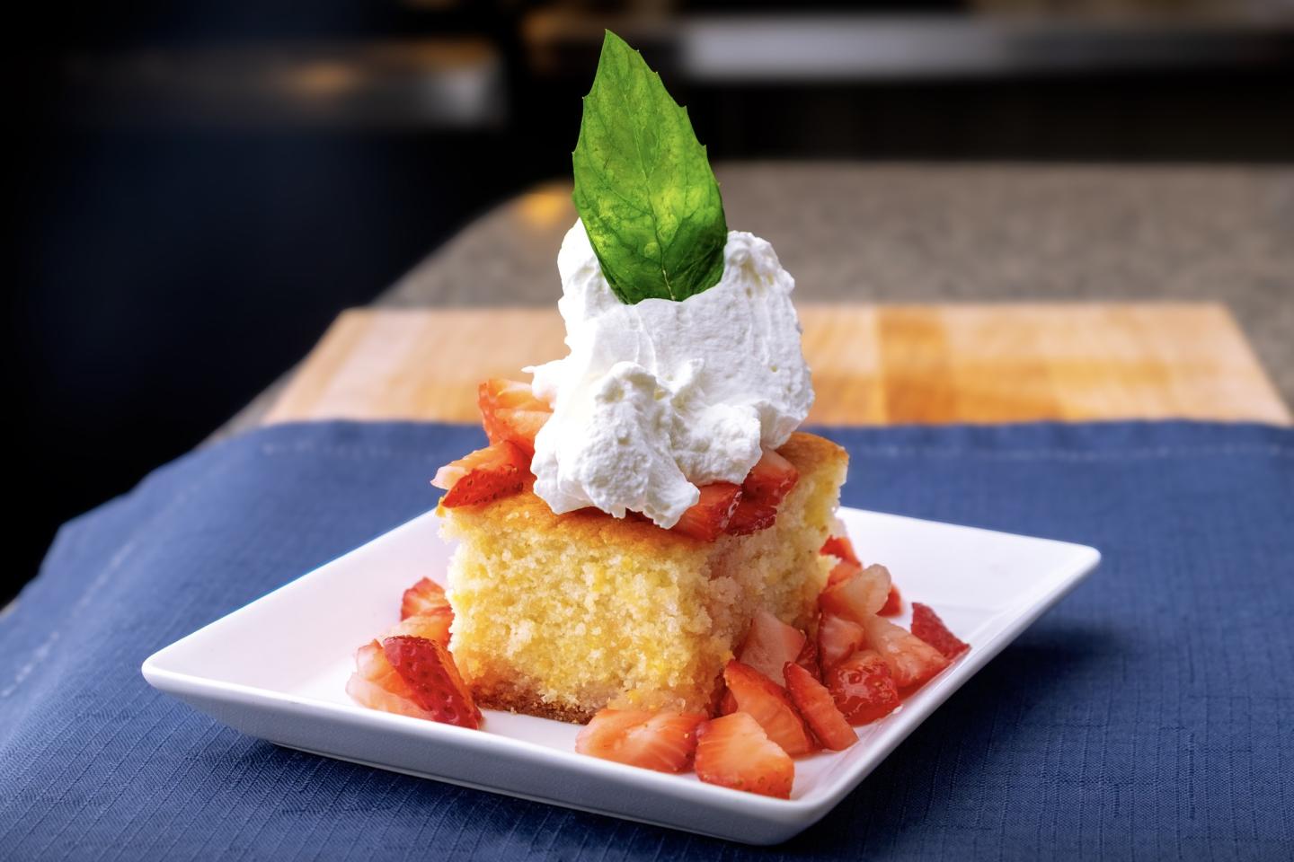 Cake topped with whipped cream, strawberries, and a mint leaf on a white plate.