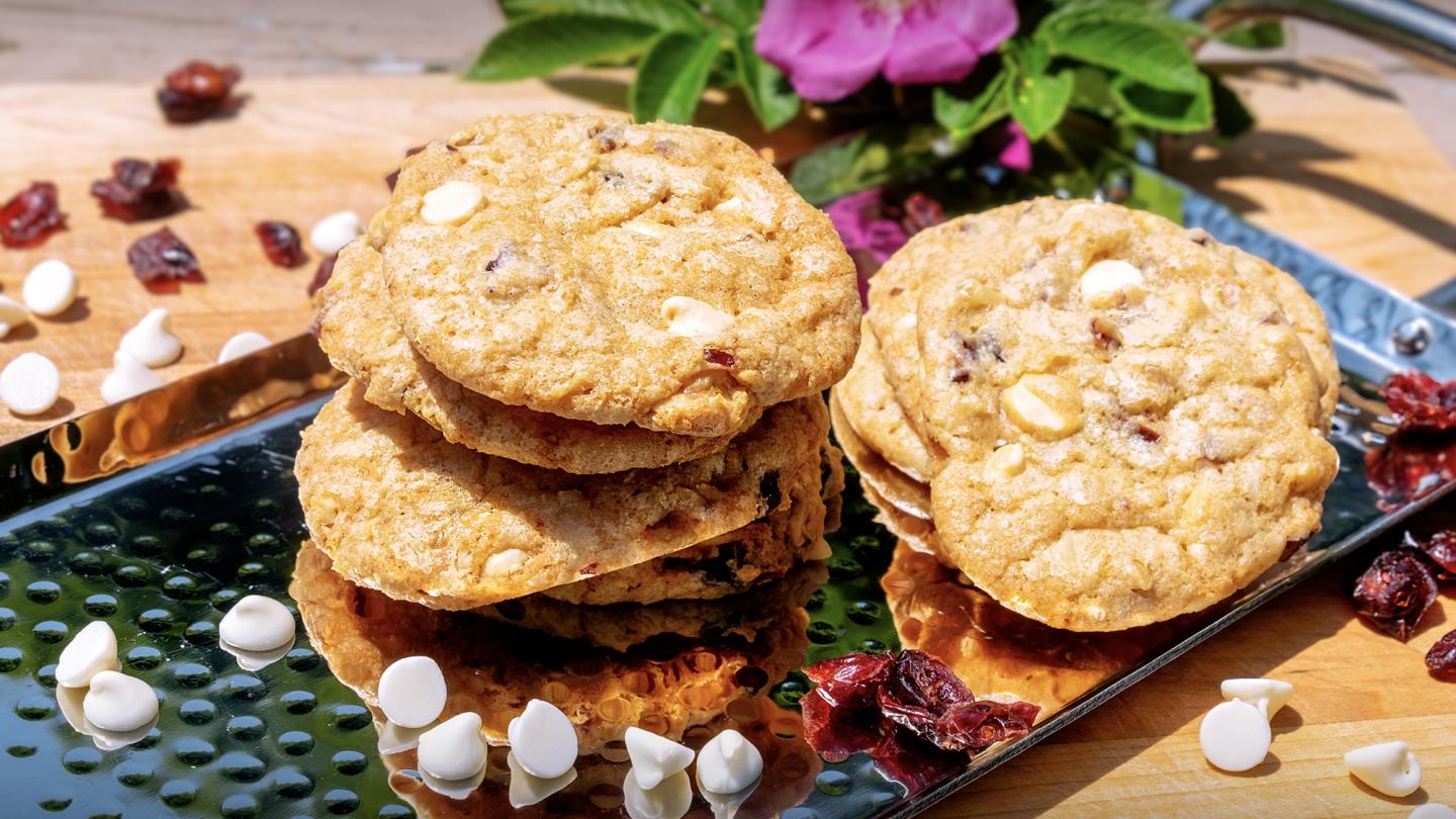 Stack of cookies with white chocolate and cranberries on a tray, floral background.