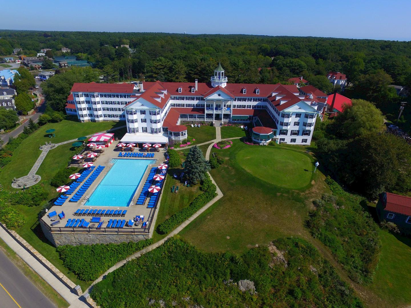 Aerial view of large red-roofed hotel with a blue swimming pool.