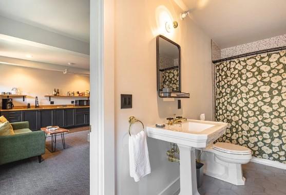 Bathroom with floral wallpaper, mirror, and white sink next to cozy living area.
