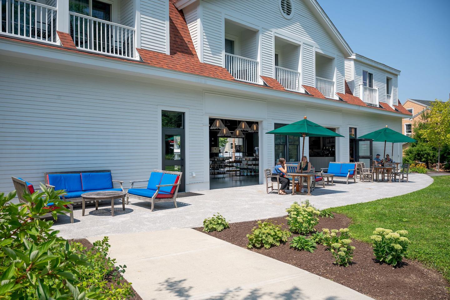 Modern courtyard with blue seating, green umbrellas, and landscaping.veside