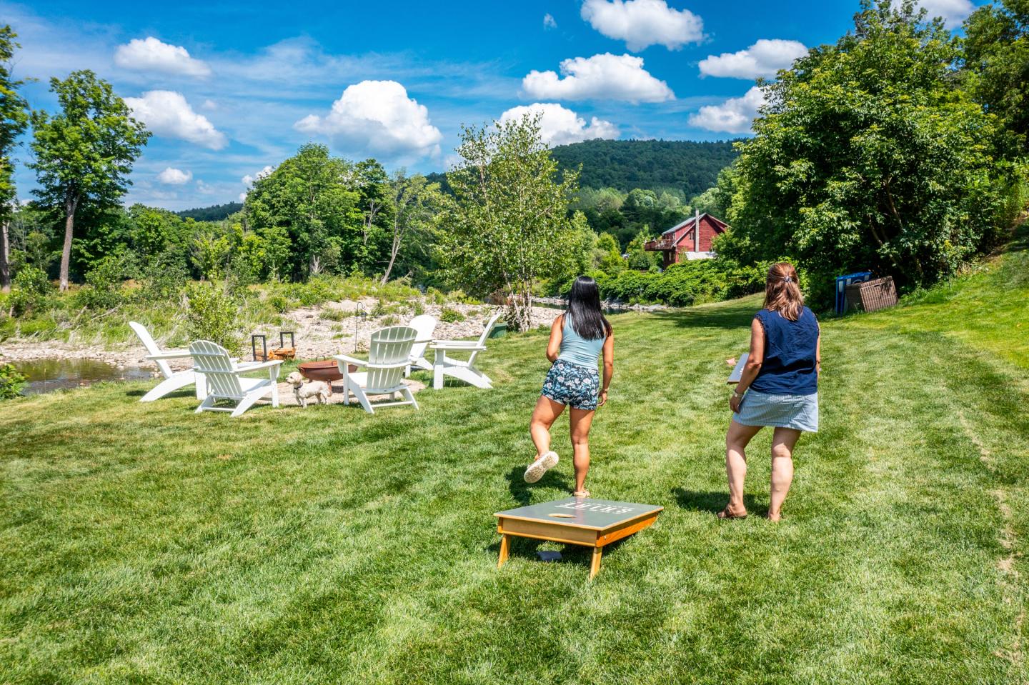 Two people playing cornhole on a grassy field under a blue sky.